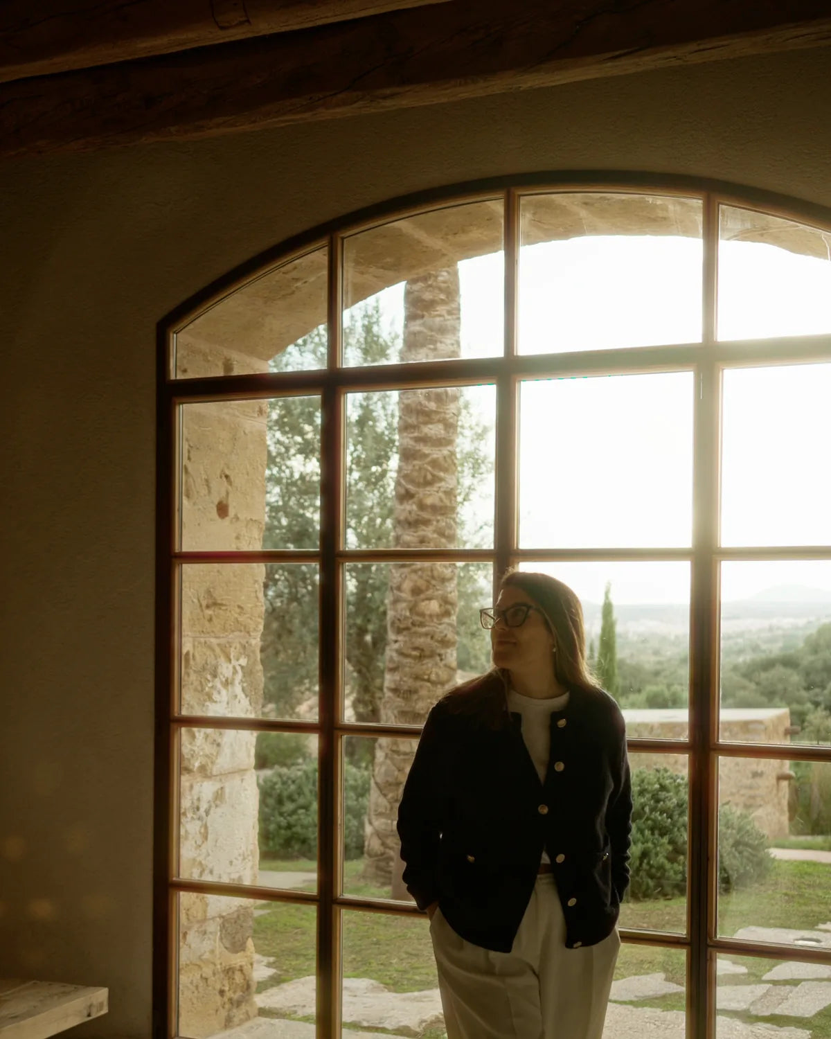 A woman before a large arched BlackFramed steel window overlooking a Tuscan landscape